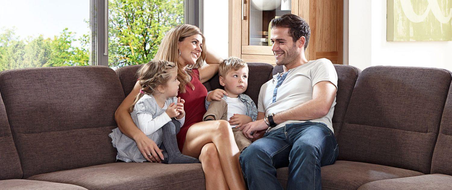 Zufriedene Familie mit zwei Kindern auf braunen Sofa