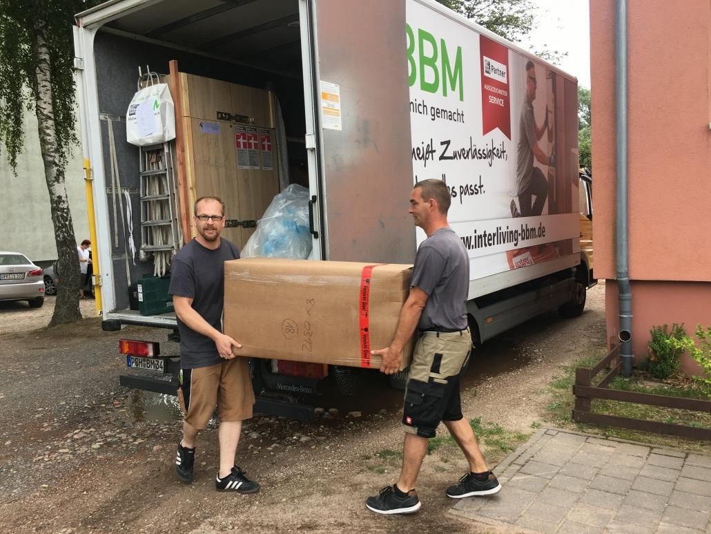Zwei BBM Mitarbeiter tragen ein verpacktes Möbelstück