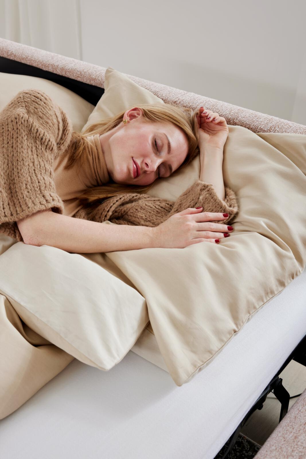 Frau schläft in beige Bettwäsche