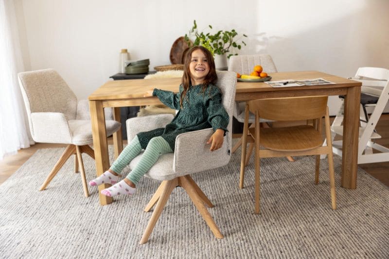 Kleines Mädchen, dass auf einem grauen Stuhl sitzt und lacht