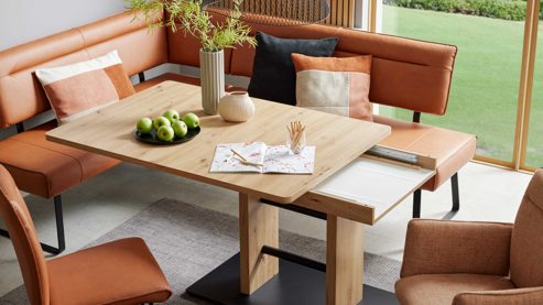 Auszugstisch interliving aus hellem Holz, Ecksofa in Lederoptik in dunklem orange im Hintergrund
