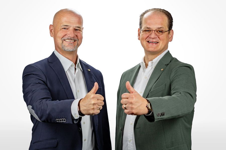 Zwei Männer zeigen lächelnd Daumen hoch und schauen in die Kamera.