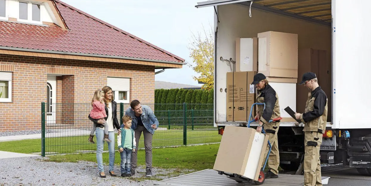Zwei Lieferanten liefern ein großes Paket, eine Familie schaut glücklich dabei zu