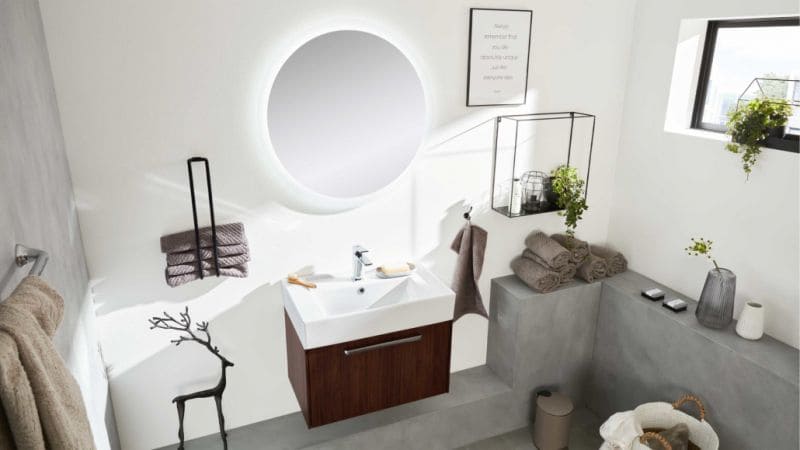 Graues Badezimmer mit rundem, beleuchtetem Spiegel, über dem Waschbecken