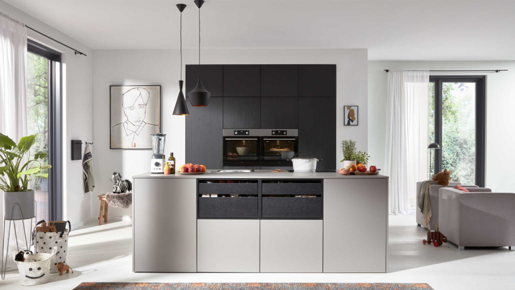 Schwarze Küche im Hintergrund, im Vordergrund eine hellgraue Kücheninsel, sehr modern und minimalitsich