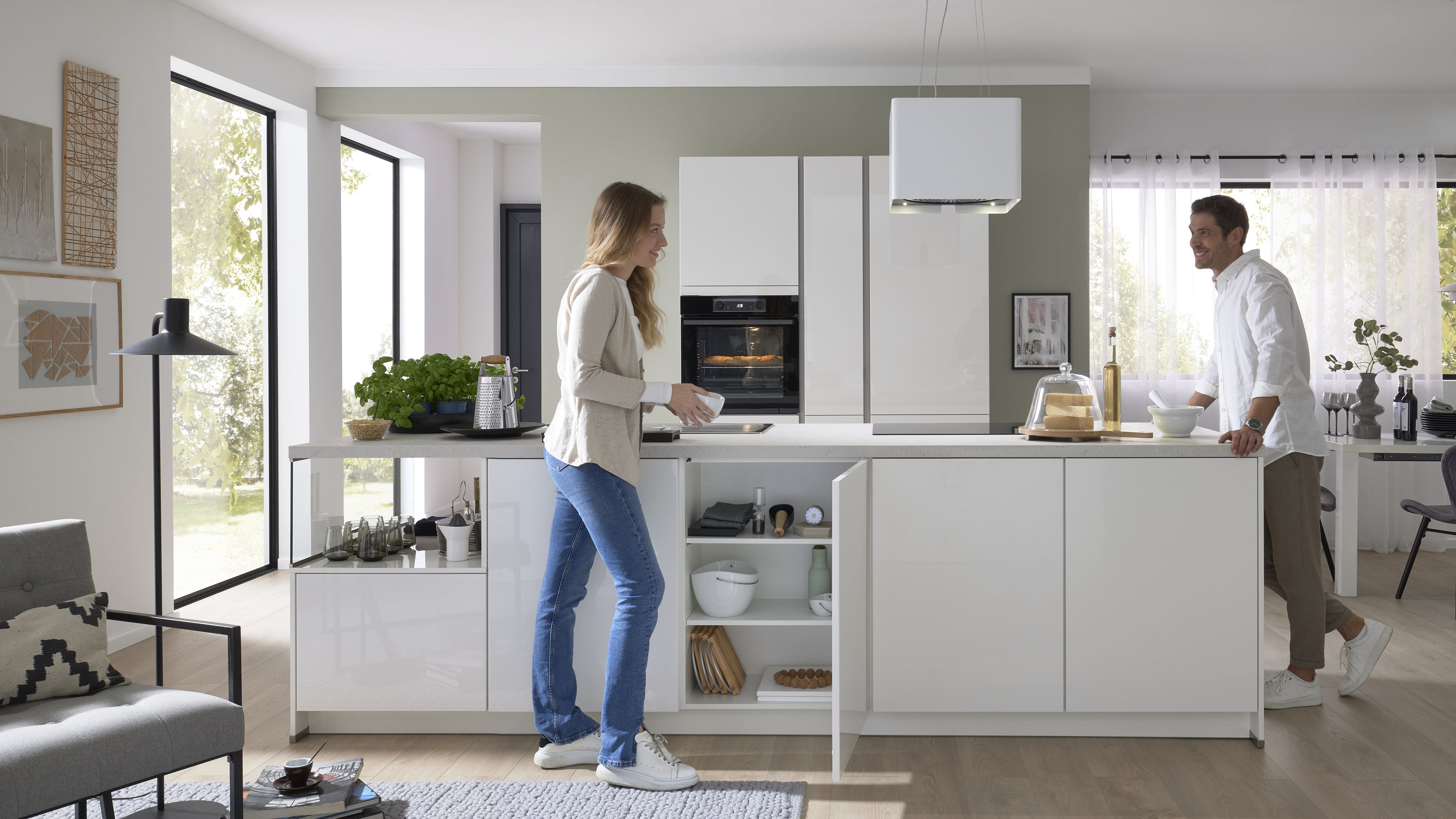 Weiße Küche in Hochglanzoptik, Mann und Frau unterhalten sich, während die Frau Geschirr einräumt