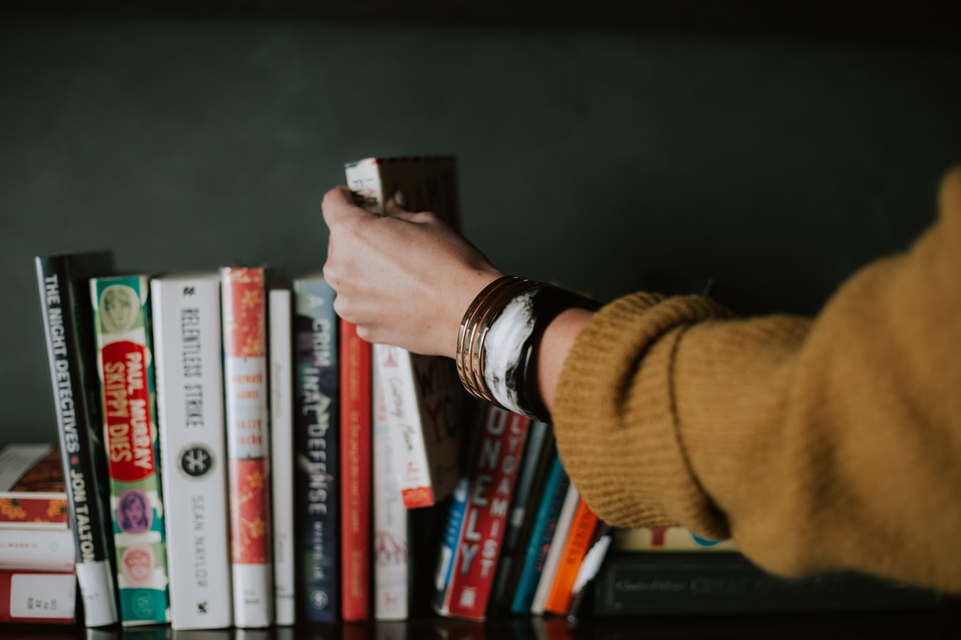 Frau holt Buch aus Bücherregal 