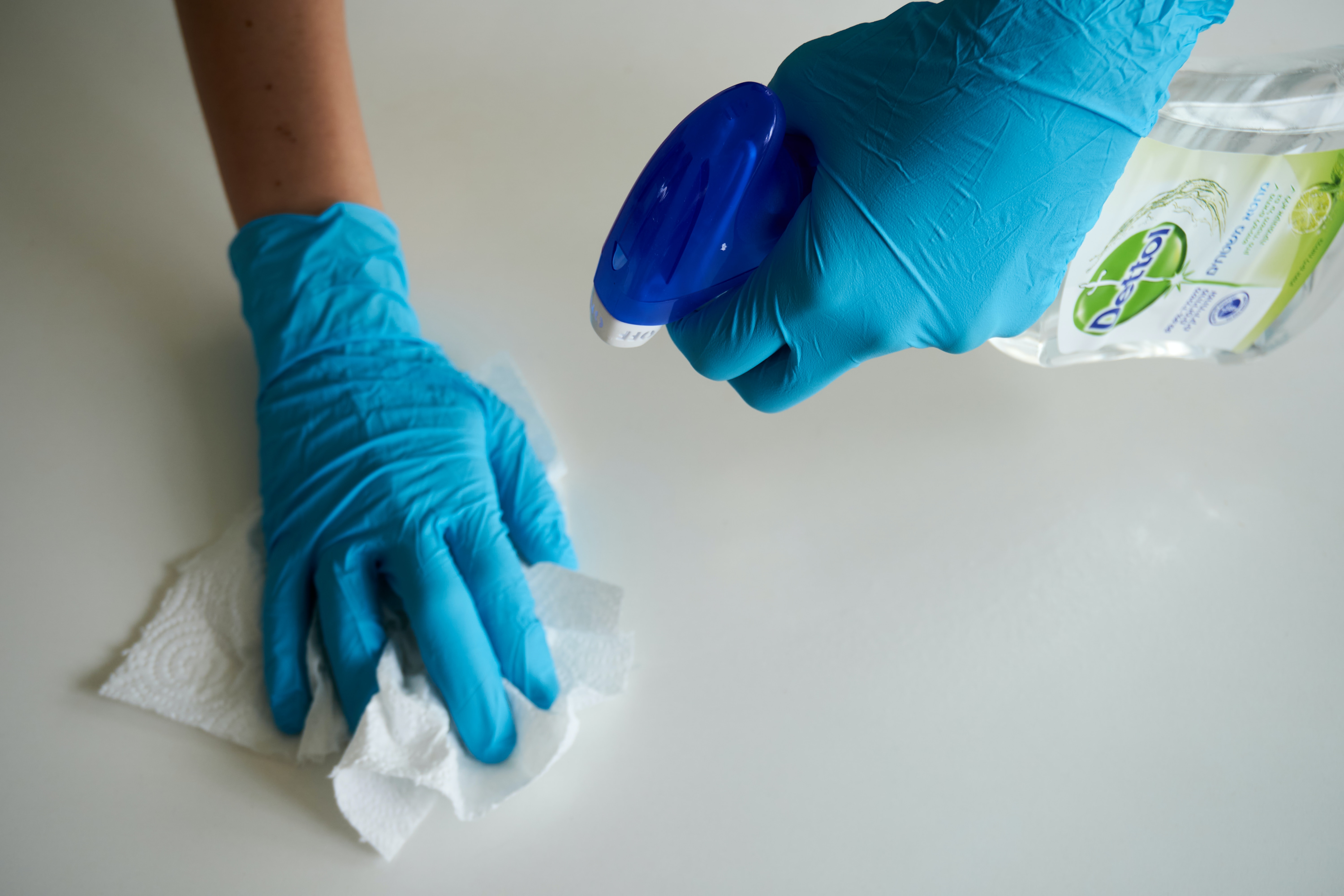 Person mit Handschuhen reinigt mit einem Reiniger eine Fläche