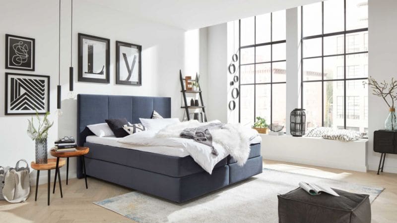 Modernes, dunkelblaues Bett mit weißer Bettdecke in einem eingerichteten Schlafzimmer