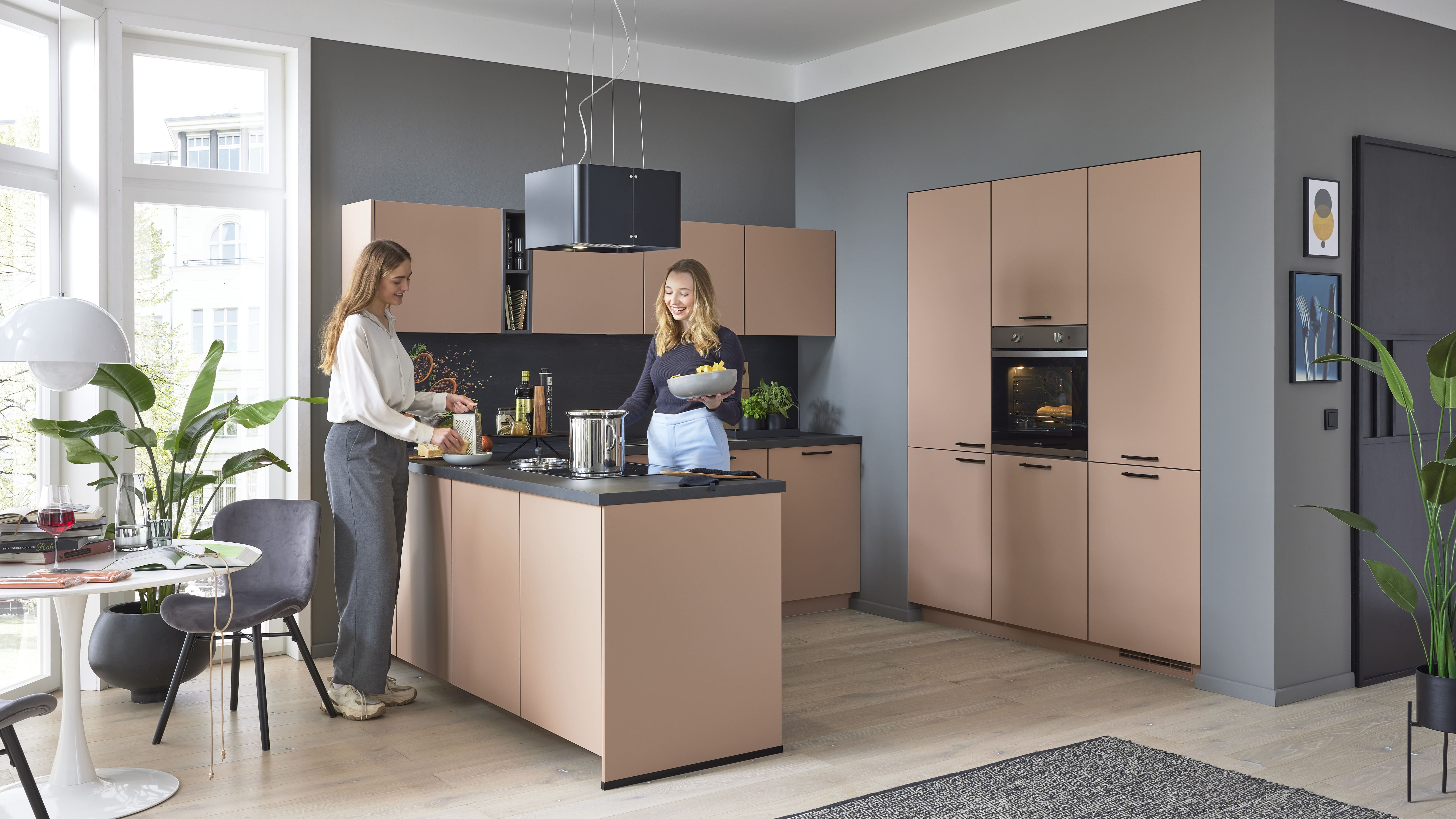 Küche in Grau und Braun, matter Stil. Zwei Frauen bereiten dort Essen zu.