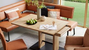 Auszugstisch interliving aus hellem Holz, Ecksofa in Lederoptik in dunklem orange im Hintergrund