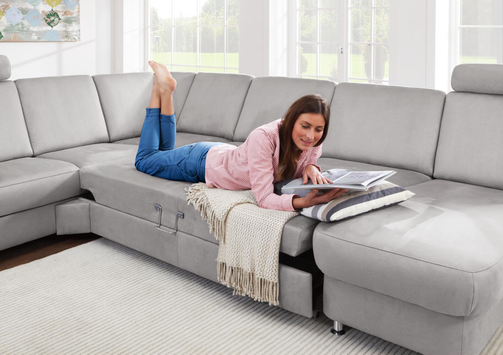 Frau ließt auf dem Bauch liegend ein Magazin auf ihrem grauen Sofa