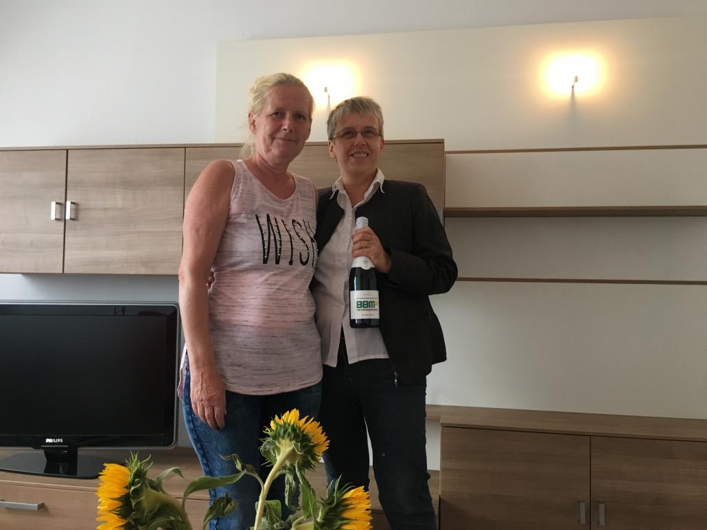 Zwei Frauen vor einer Wohnwand in Holzoptik lächeln in die Kamera