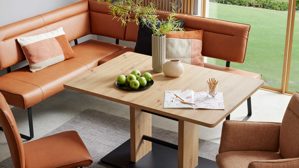 Auszugstisch interliving aus hellem Holz, Ecksofa in Lederoptik in dunklem orange im Hintergrund
